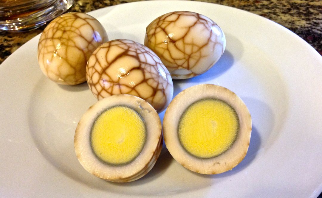 Готовые чайные (мраморные) яйца, одно из которых разрезано, на блюде
